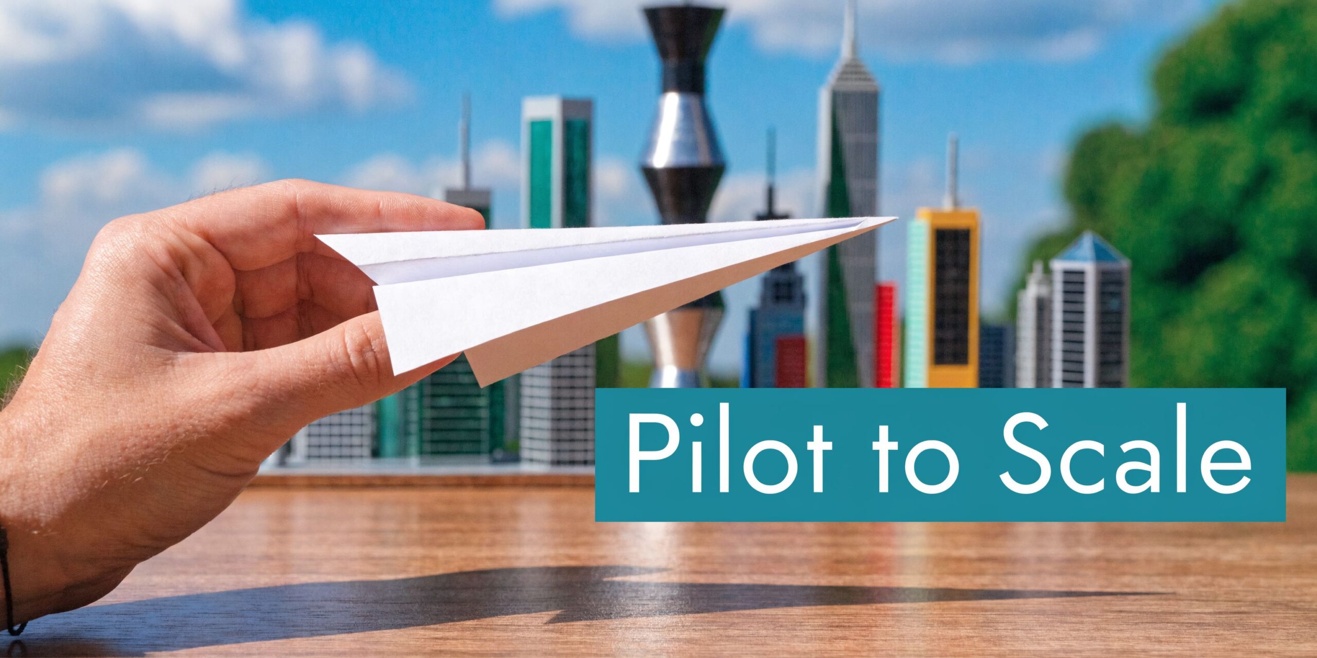 A hand holding a paper airplane in front of a miniature cityscape representing business development.