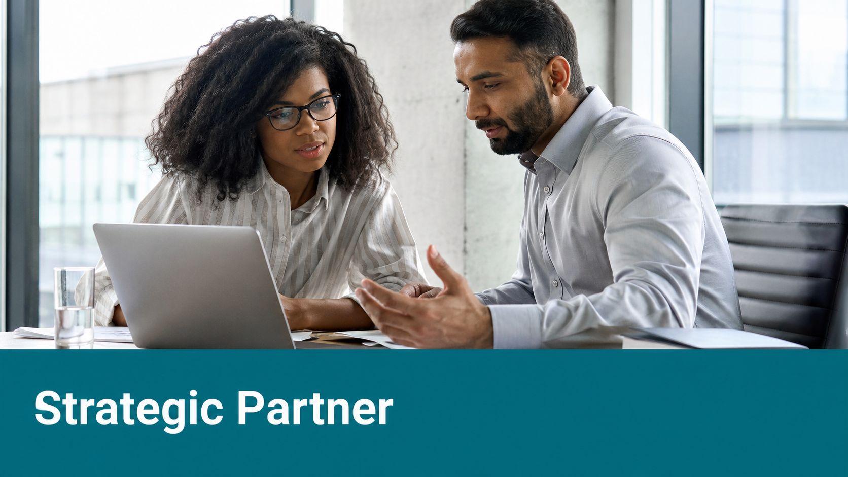 A professional man and woman working together on a laptop in a bright, modern office setting.